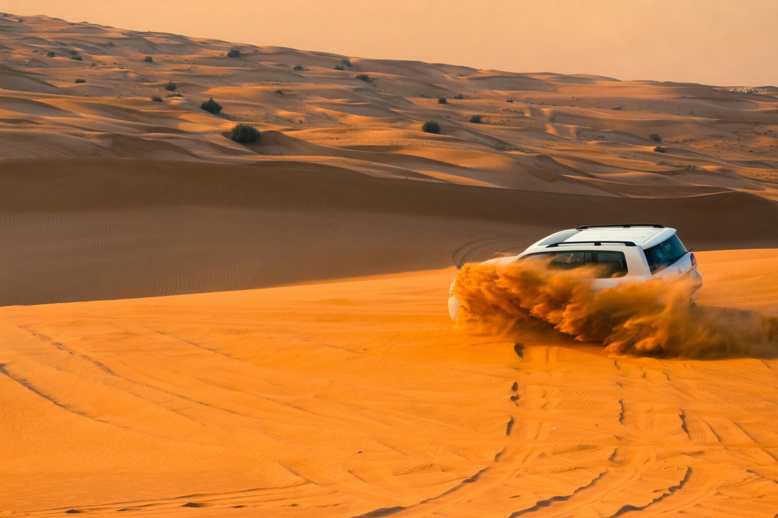 An SUV driving over sand dunes in the Dubai desert, with sand spraying as it moves