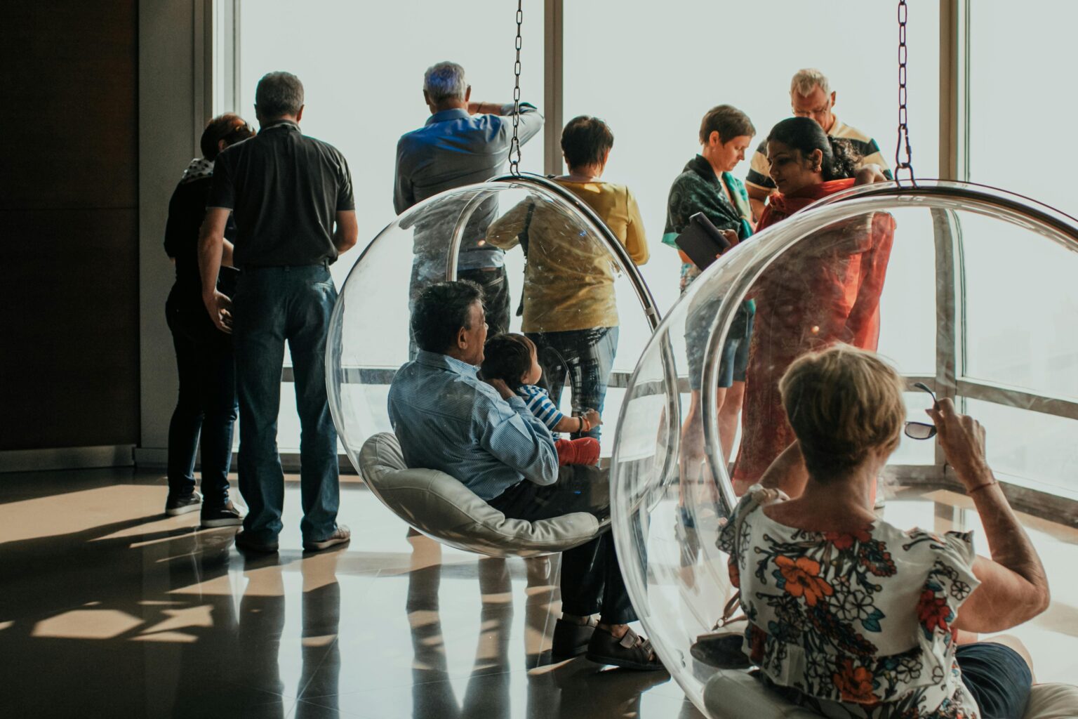 Two people sitting on transparent chairs at the Burj Khalifa observation deck, with a stunning view of Dubai from above